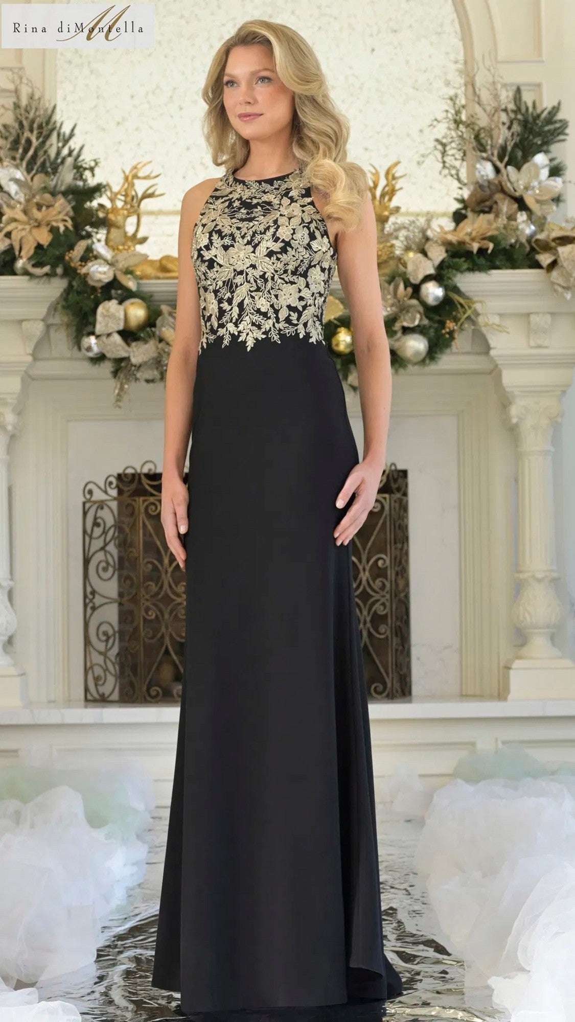 A woman stands indoors in front of a decorated mantle, wearing the Rina Di Montella RD3345 long formal dress with a stretch crepe fabric and an ornate gold floral embroidery bodice.
